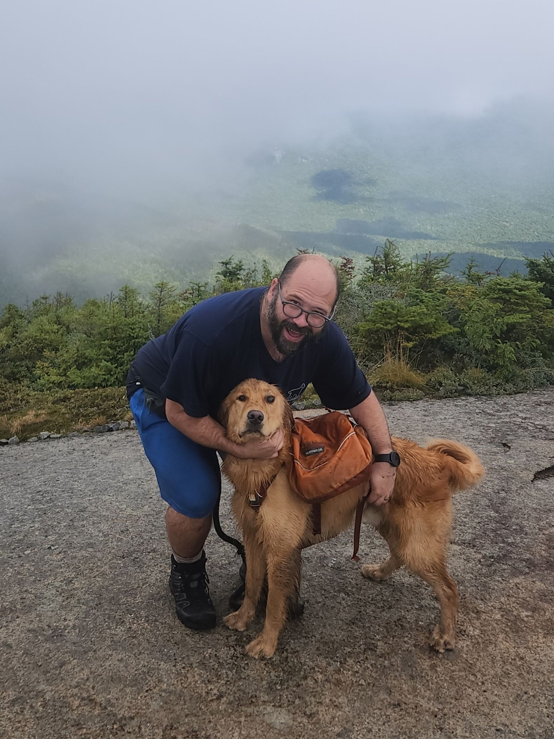 Adam crouches beside Sunny on the cloud-covered summit of Gothics.