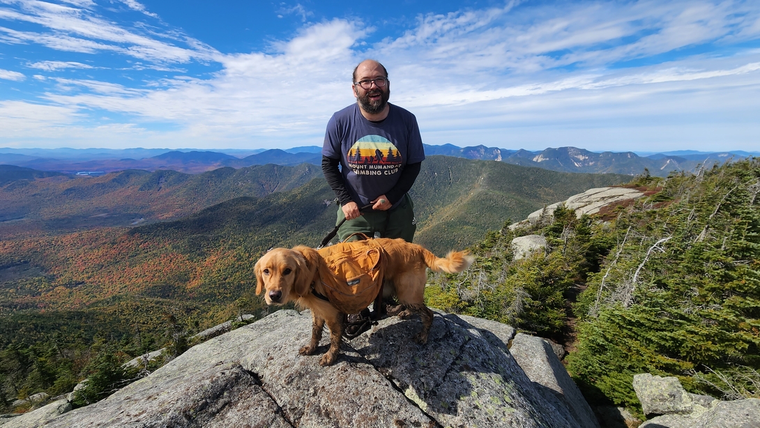 Adam and Sunny pose on Dix Mountain with the autumn-colored Colvin Range behind them.