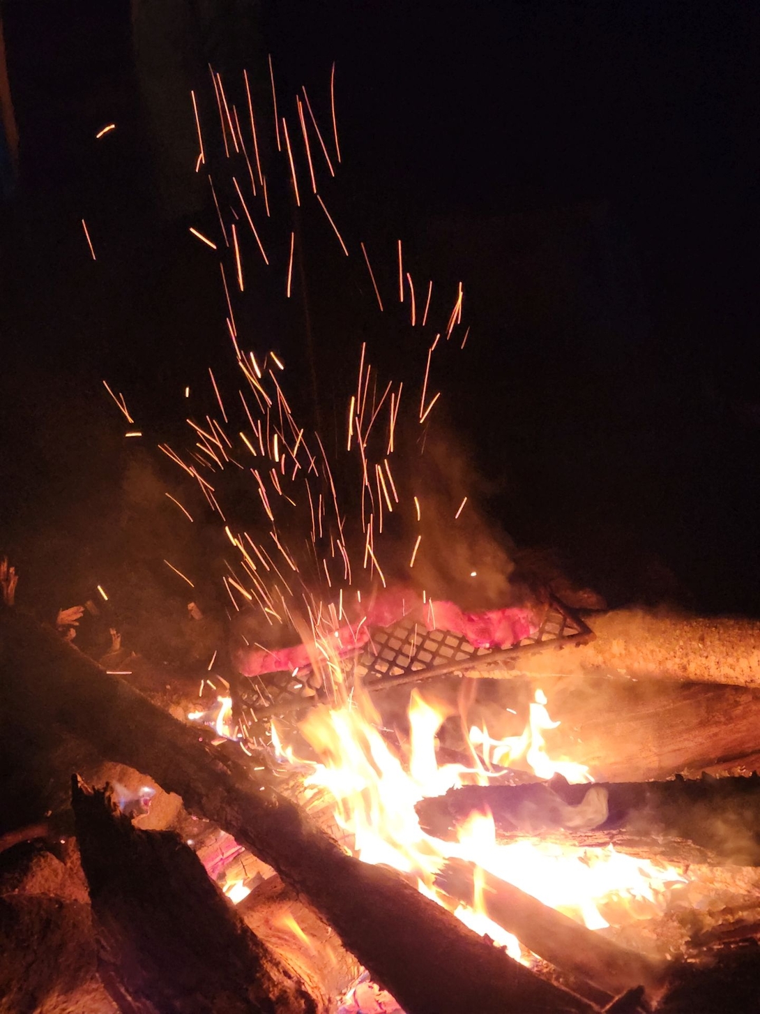 A lively campfire burns beneath a cooking grill at the snowy Cranberry Lake campsite.