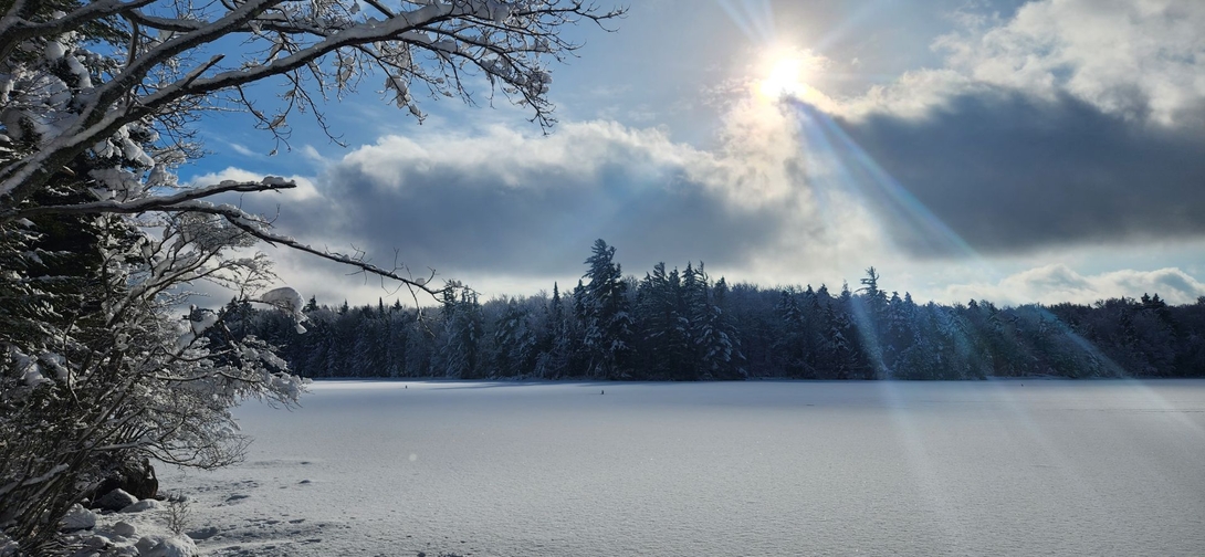 Sunbeams break through winter clouds above the snow-covered expanse of Cranberry Lake.