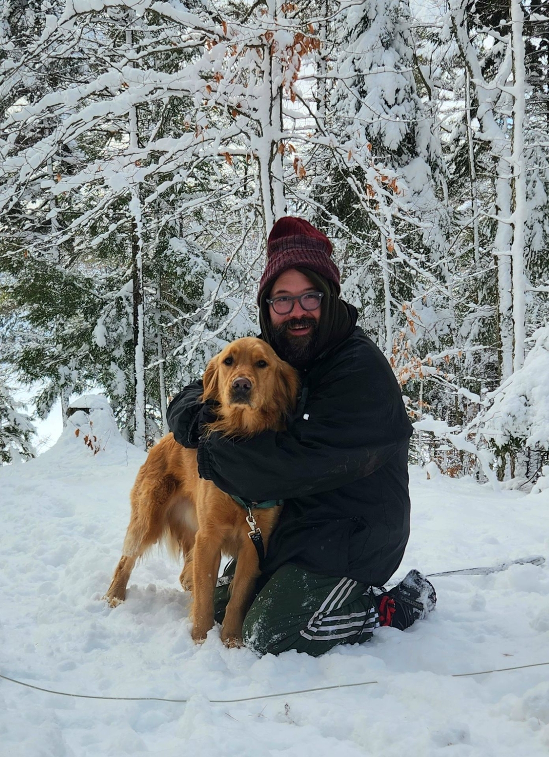 Adam kneels to hug Sunny in the snow-covered forest near Cranberry Lake.