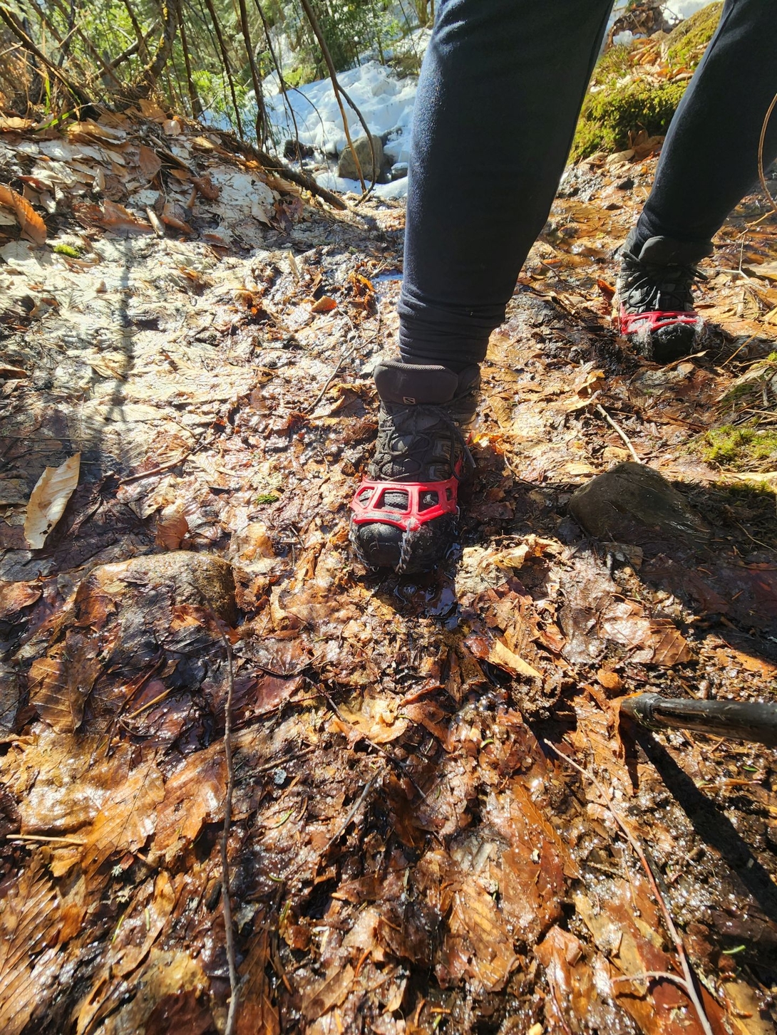 Adam wears red traction spikes on the wet, icy trail.